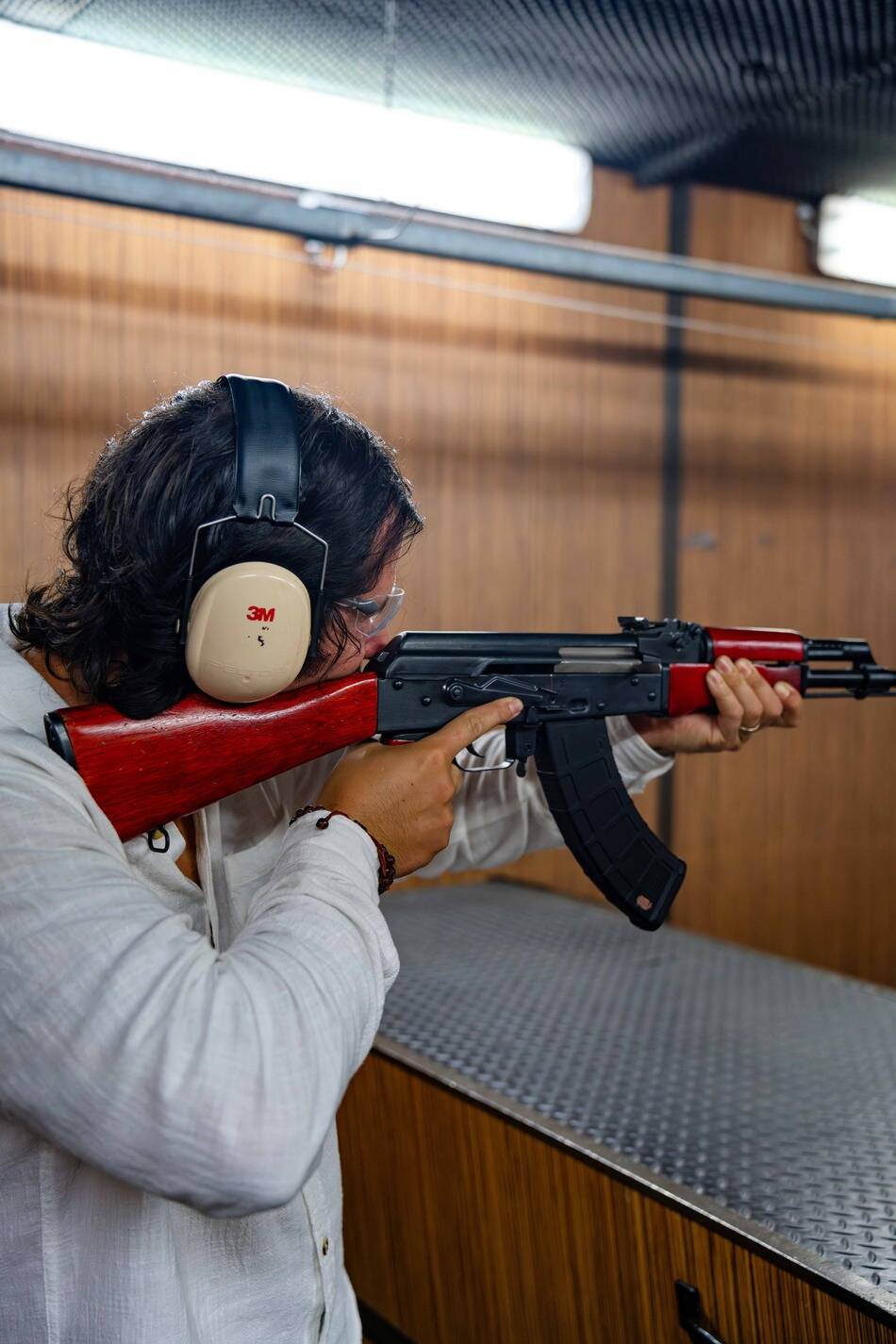 Gun Fun Terms and Conditions: Man holding a semi-automatic rifle whilst aiming for a target in one of Gun Fun's indoor shooting bays.